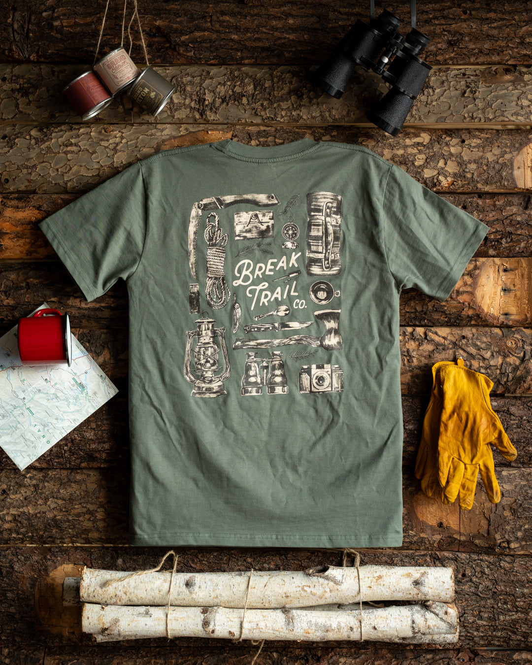 Green t-shirt with graphic design on a wooden surface with outdoor gear.
